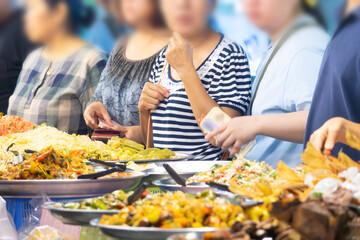 A group of people are standing around a buffet table with a variety of food. Scene is casual and...