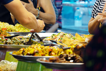A group of people are gathered around a table with a variety of food, including a plate of salad