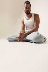 Fototapeta premium Portrait of confident young bearded man posing in the studio sitting n the floor. Mind set and mental health.