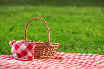 One picnic wicker basket with checkered napkin and blanket on green grass. Space for text