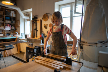 Woman carpenter prepares wooden blocks for work, apply tape before gluing parts together, setting up clamp in workshop. Female artisan focus on craftsmanship, tool usage, assembly, woodworking skills