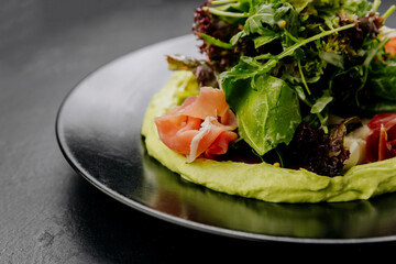 Fresh salad with avocado cream and prosciutto, served on a black plate, perfect for gourmet dining