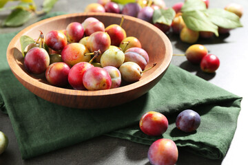 Ripe plums in bowl on grey table, closeup