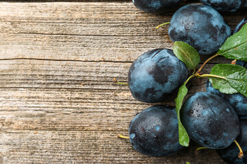 Tasty ripe plums and leaves on wooden table, flat lay. Space for text