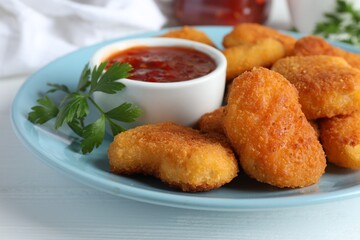 Tasty chicken nuggets with chili sauce and parsley on white table, closeup