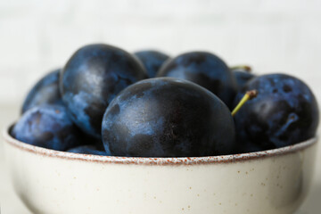 Ripe plums in bowl on table, closeup