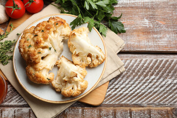 Plate with tasty baked cauliflower and products on wooden table, flat lay. Space for text