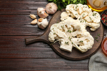 Uncooked cauliflower steaks, oil and spices on wooden table, flat lay