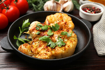 Tasty cauliflower steak in frying pan and other products on wooden table, closeup