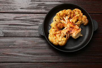 Tasty cauliflower steak in frying pan on wooden table, top view. Space for text