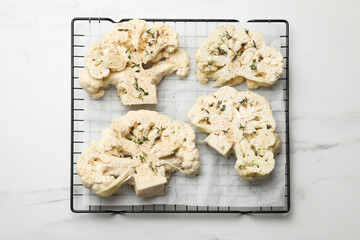 Uncooked cauliflower steaks and dill on white marble table, top view