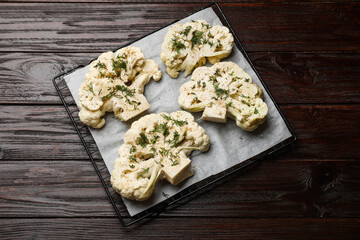 Uncooked cauliflower steaks and dill on wooden table, top view