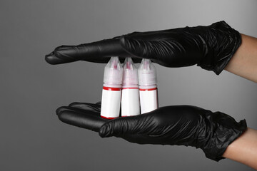 Professional cosmetologist holding bottles of pigments for permanent makeup on grey background,...