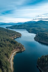 Obraz premium A beautiful mountain range with a river running through it. The sky is clear and blue, and the water is calm. The trees are lush and green, and the landscape is serene and peaceful