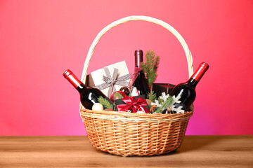 Wicker gift basket with wine on wooden table against pink background