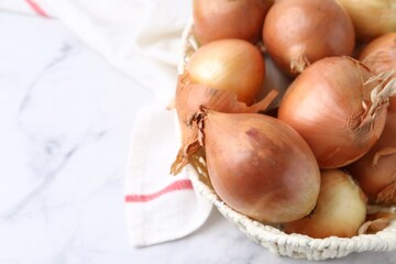 Fresh onions with peels in wicker basket on light marble table, above view. Space for text