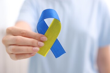 Woman with yellow and blue ribbon on light background, closeup. Down syndrome awareness