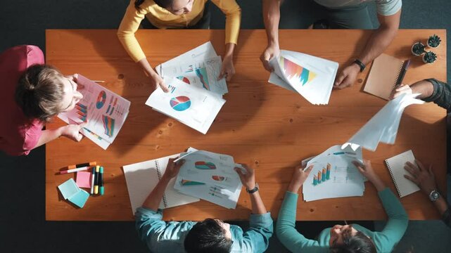 Top view of smart people throw paper and giving high five at meeting table with financial document and stock market analysis paper scattering around. Aerial view of team celebrate project. Symposium.
