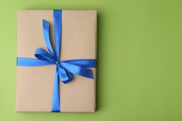 Gift box with blue bow on green background, top view. Space for text