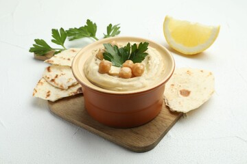 Delicious hummus with parsley, chickpeas, pita and lemon on white table, closeup