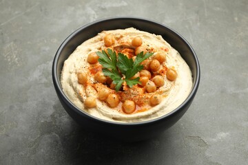 Delicious hummus with parsley, paprika and chickpeas in bowl on grey table, closeup