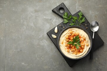 Delicious hummus with parsley, paprika and chickpeas on grey table, top view. Space for text