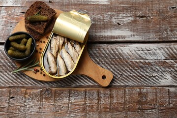 Tasty sprats in tin can served on wooden table, top view. Space for text