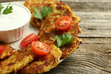 Delicious potato pancakes, sour cream, tomatoes and parsley on wooden table, closeup
