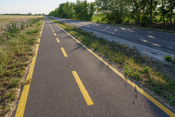Straight cycle path and country road side by side, with trees and shadows, backlit, countryside, wide angle lens