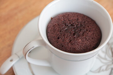 Close up the Chocolate Mug Cake. Cake in a white cup on the wooden coffee table. Chocolate cake cooked in a cup. Easy and practical dessert.