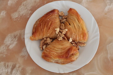 Three pieces Turkish baklava with walnuts on a white plate. Baklava folded in the form of mussels. Homemade baklava presentation and service. Traditional turkish dessert. Top view