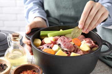 Woman preparing stew with vegetables and meat at white tiled table, closeup