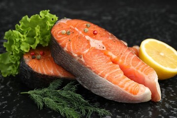 Fresh raw salmon steaks with spices, lemon, lettuce and dill on dark textured table, closeup