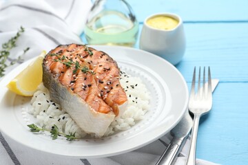 Tasty grilled salmon steak with rice, thyme, lemon and sesame seeds on light blue wooden table, closeup