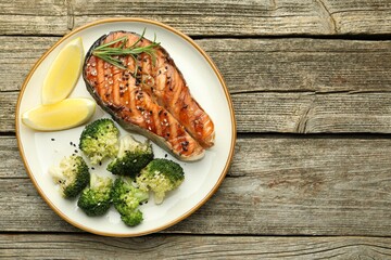 Tasty grilled salmon steak, broccoli, lemon and rosemary on wooden table, top view. Space for text