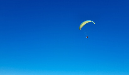 A paraglider with a blue parachute fly. A male flyght on the sky and lifts a paraglider into the air