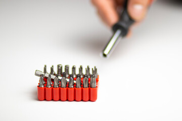 A close-up shot of a screwdriver bit set in an orange holder, with a blurred hand holding a tool in...