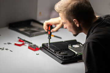 A man repairs a console, using a screwdriver to carefully open the device, focusing on its internal components and fan system.