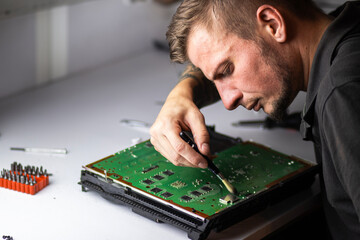 A man works intently on a board, using a brush to clean it. He carefully inspects the parts while...