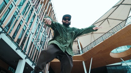 Low angle view of hipster pose in hip hop style surrounded by mall view. Portrait of sporty asian hip hop choreographer dancing break dance while looking at camera. Outdoor sport 2024. Hiphop.