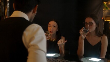 Portrait of VIP guest in beautiful woman making a toast in cheers at luxurious nightclub at vibrant nightlife party. Sitting at counter bar talking with barman atmosphere party lifestyle. Vinosity.
