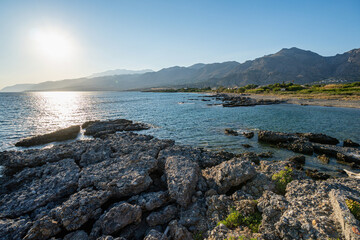 Empty rocky beach at sunset, clear blue sky, backlit, Greece, Crete island, wide angle lens