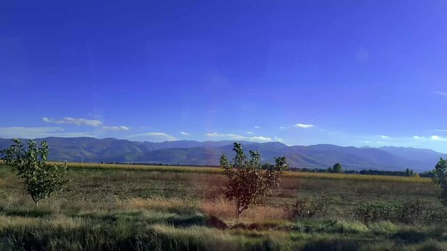 Horizontal 4K video. View of mountains, blue sky, field, highway, tree, grass from car window. Road to Tbilisi from Borjomi. Georgia. Route taxi. Way. Concept of travel, tourism, road tripю Sunny day