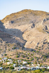 Houses of a small village at the foot of a high, barren, rocky mountain, in sunshine, with a clear blue sky, telephoto