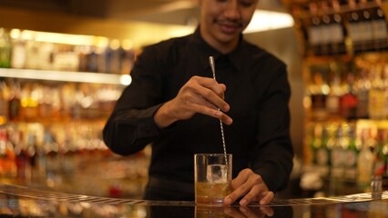 Smart Asian bartender holding stirring mixed alcohol syrup into glass with ice for on the rock served mixing at bar. Special refresh drink showcasing nightlife mixology at luxury nightclub. Vinosity.