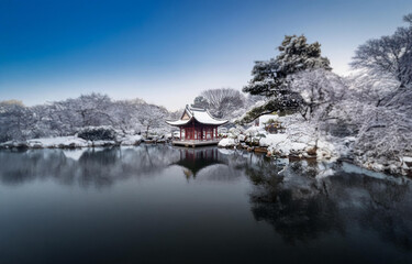 Fototapeta premium A red wooden pavilion in a snow covered forest, reflected in still water.