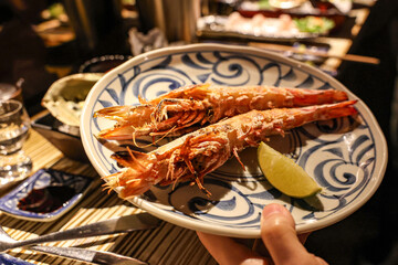Grilled Prawns with Lime Wedge on Artistic Plate. Two large grilled prawns, beautifully presented on a decorative plate with a blue swirl pattern.
