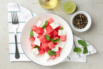 Delicious watermelon salad with mint and feta cheese in bowl served on grey textured table, flat lay
