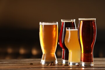 Glasses with different types of beer and pistachio nuts on wooden table indoors, space for text