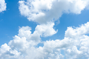 Fluffy cumulus clouds drift across a bright blue sky, painting a beautiful summer day